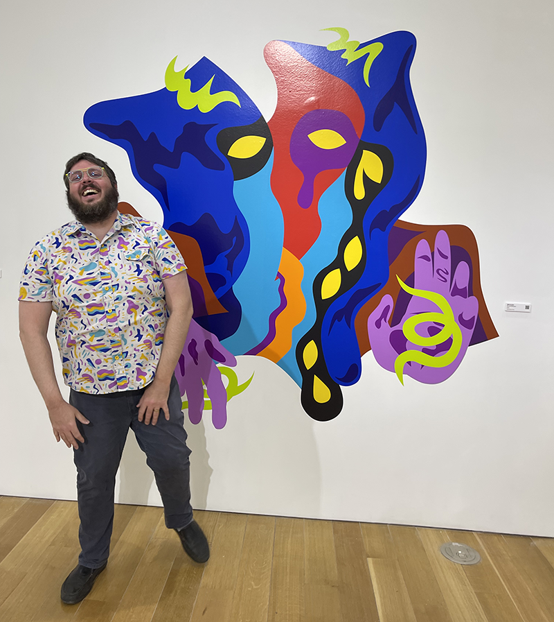 Will Cardini at the Read the Room opening, laughing in front of his colorful vinyl mural