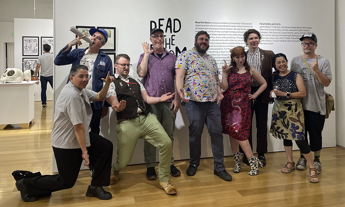 Group of artists making silly poses in front of the entry wall of the exhibition Read the Room